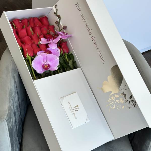Boxed arrangement of red roses and pink orchids with a greeting card