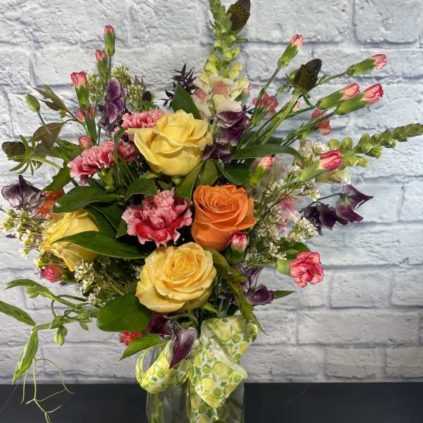 Mixed bouquet of roses, carnations, and snapdragons in a glass vase