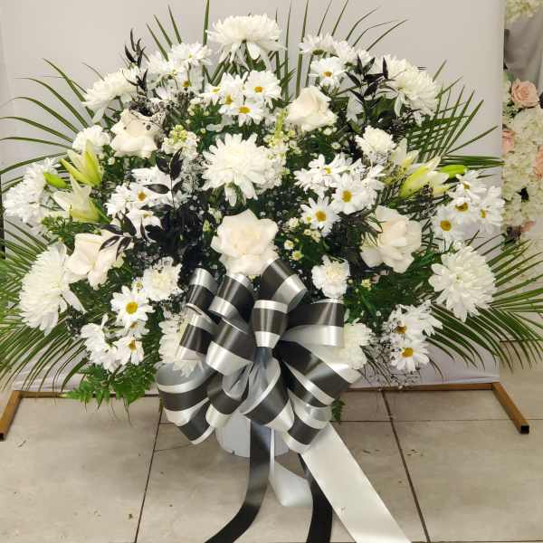 Large white floral spray with daisies, roses, and a black-and-white ribbon bow