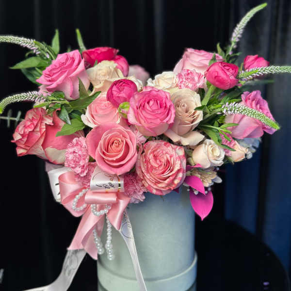 Pink and white roses arranged in a round hatbox with ribbon and pearl accents