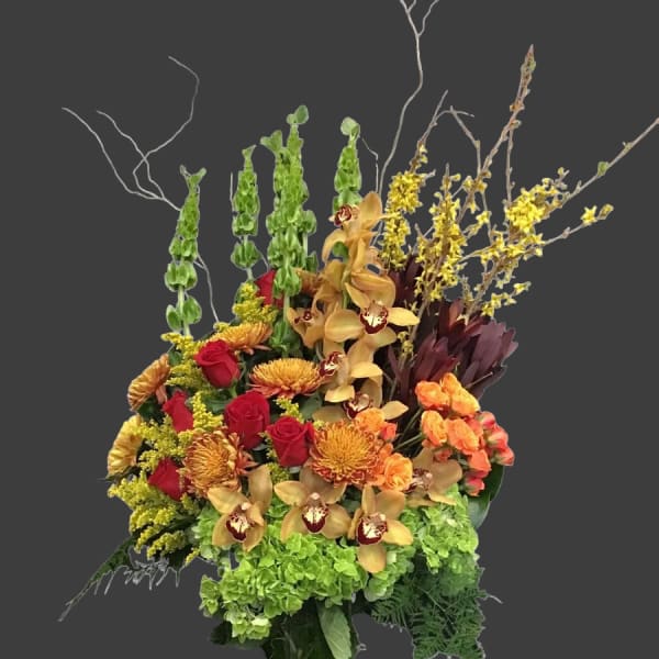 Tall mixed bouquet with red roses, orchids, and green hydrangeas in a wrapped vase