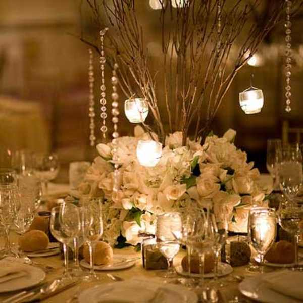 White floral centerpiece with hanging candle lights on a banquet table