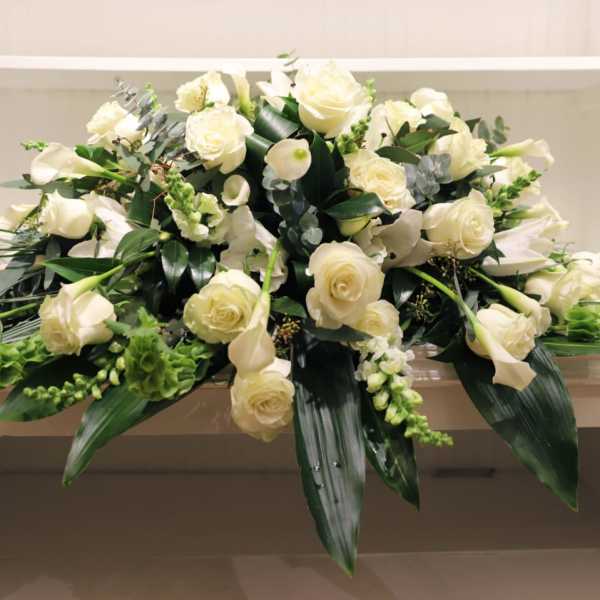 White rose and calla lily arrangement with greenery in a low container