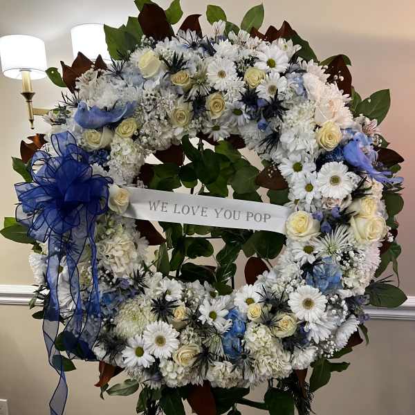 Large floral wreath with white and blue flowers and a ribbon banner