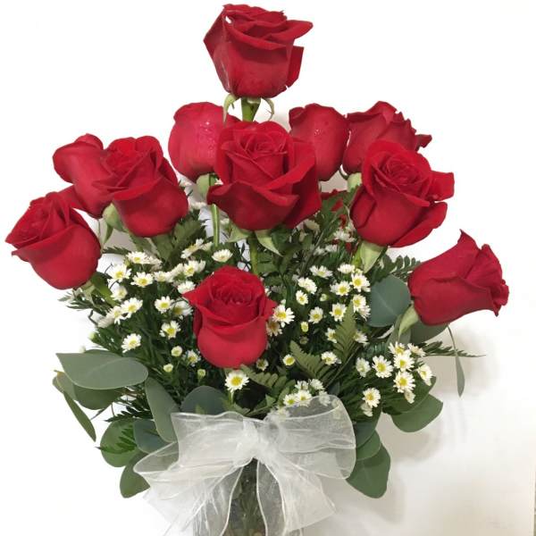 Red roses arranged in a glass vase with a white ribbon