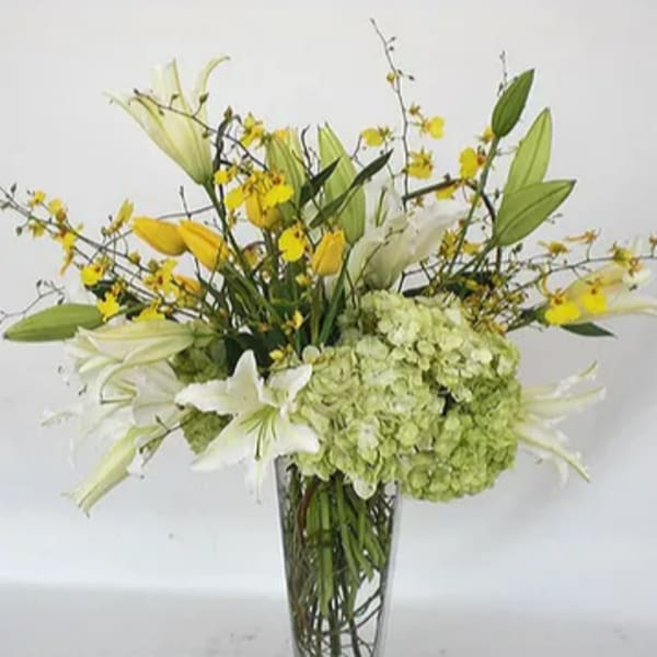 White lilies and green hydrangeas in a tall glass vase with yellow accents