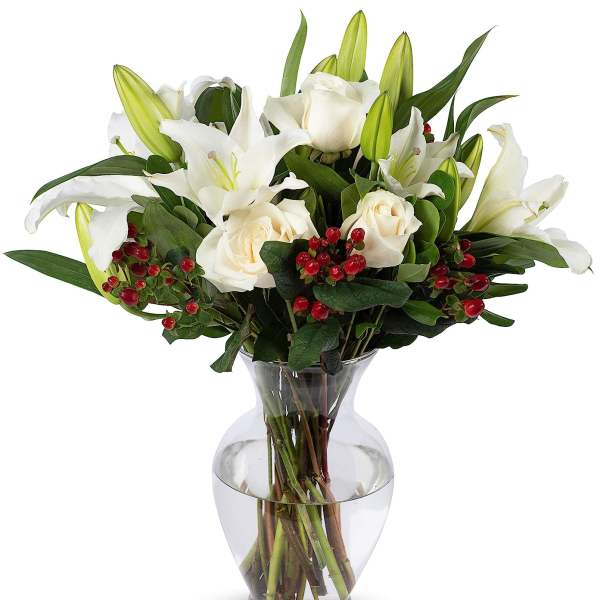 White lilies and roses with red berries arranged in a clear glass vase