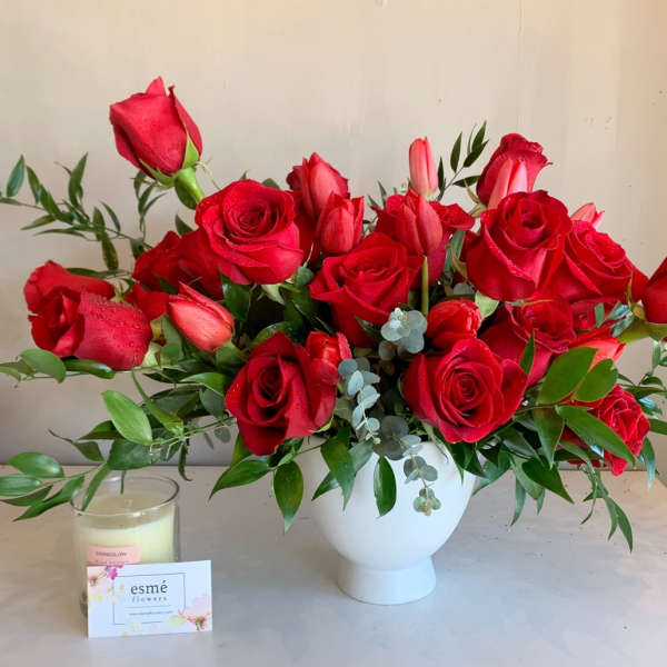 Red roses arranged in a white vase with greenery