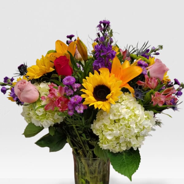 Tall mixed bouquet with sunflowers, roses, lilies, hydrangeas and purple flowers in a clear glass vase