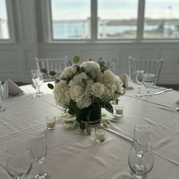 White rose and hydrangea centerpiece in a dark vase on a table