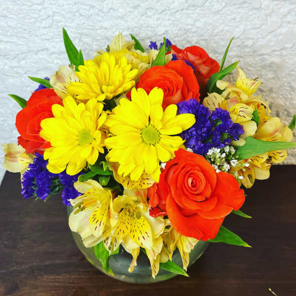 Bright mixed bouquet with yellow daisies and orange roses in a glass vase