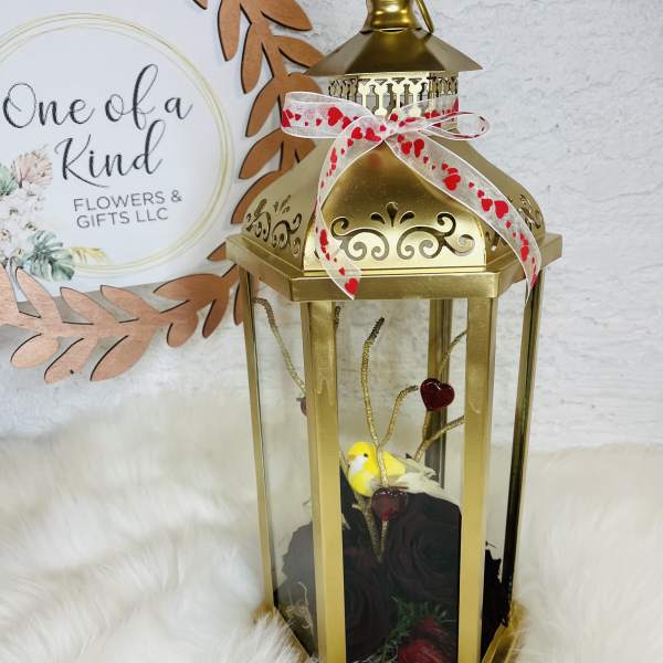 Gold lantern with a ribbon, small bird, and dark roses inside