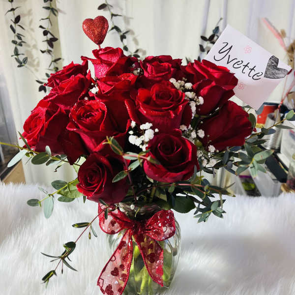 Red rose bouquet in a glass vase with a heart pick and ribbon