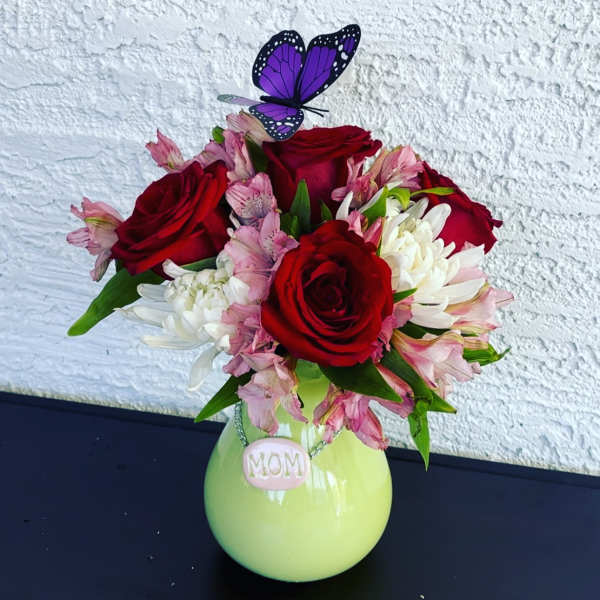 Red roses and pink-white flowers in a green vase with a butterfly topper