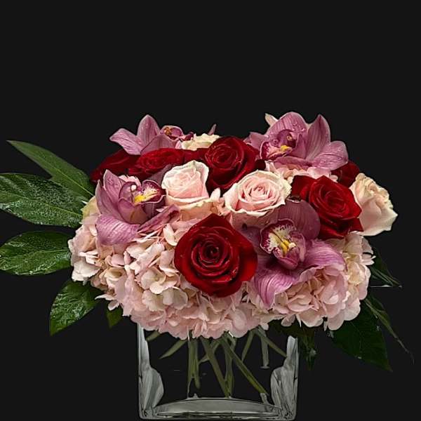 Bouquet of red and pink roses with orchids in a clear glass vase