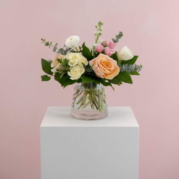 Mixed roses in a clear glass vase on a white pedestal