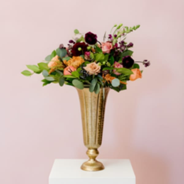 Mixed flower arrangement in a gold vase on a white pedestal