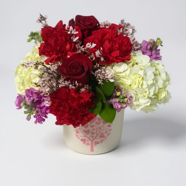 Bouquet of red roses, carnations, and hydrangeas in a cream vase