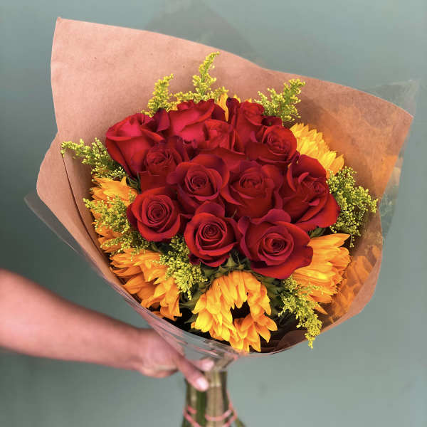Bouquet of red roses and yellow-orange flowers wrapped in brown paper