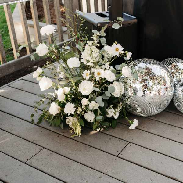 White floral arrangements with silver disco balls on a deck