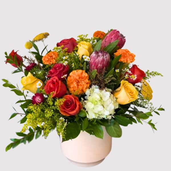 Mixed bouquet of roses, hydrangea, and protea in a pale vase