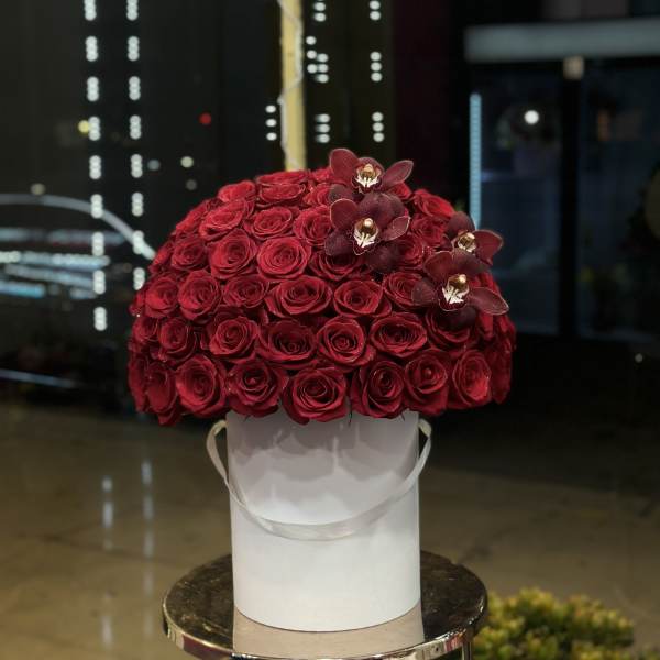 Red rose arrangement in a white hatbox with dark orchids