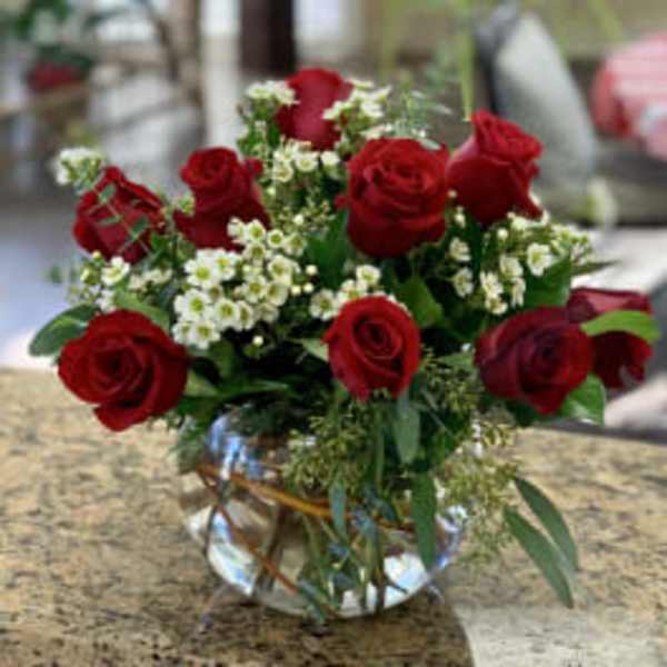 Red roses arranged in a clear glass vase with small white filler flowers