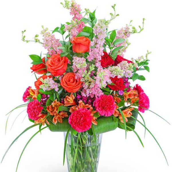Mixed bouquet of roses, carnations, and pink filler flowers in a glass vase