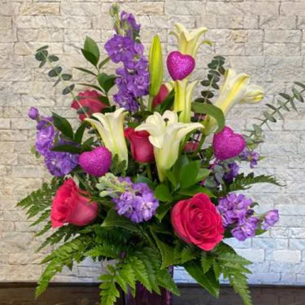 Bouquet of pink roses, white lilies, and purple flowers in a purple vase