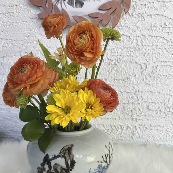 Orange ranunculus and yellow daisies in a ceramic vase