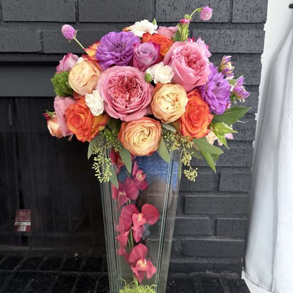 Tall floral arrangement in a clear glass vase with pink, orange, and purple blooms