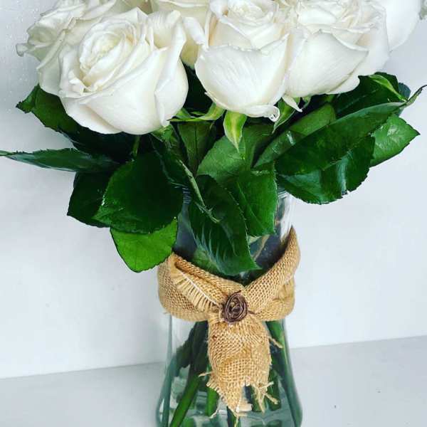 White roses arranged in a glass vase with a burlap ribbon