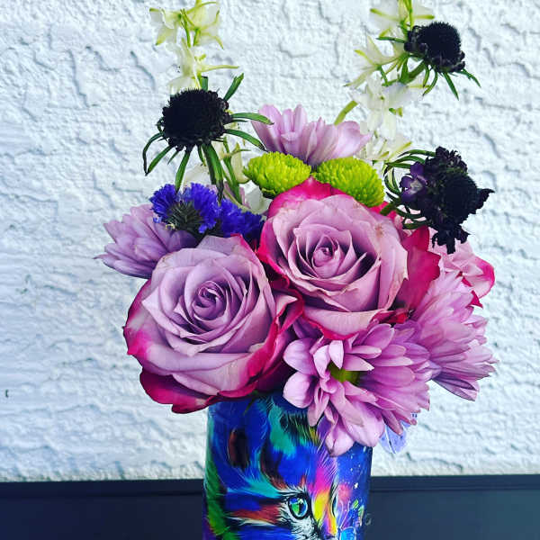 Bouquet of purple roses and mixed blooms in a colorful cat-print vase