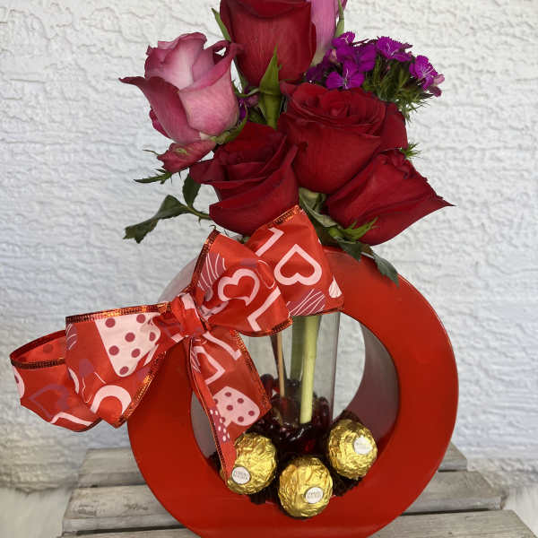 Red and pink roses in a red heart-shaped vase with a ribbon and chocolates