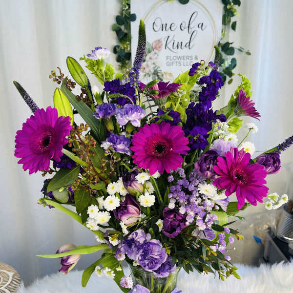 Mixed purple and pink bouquet in a glass vase with a polka-dot ribbon