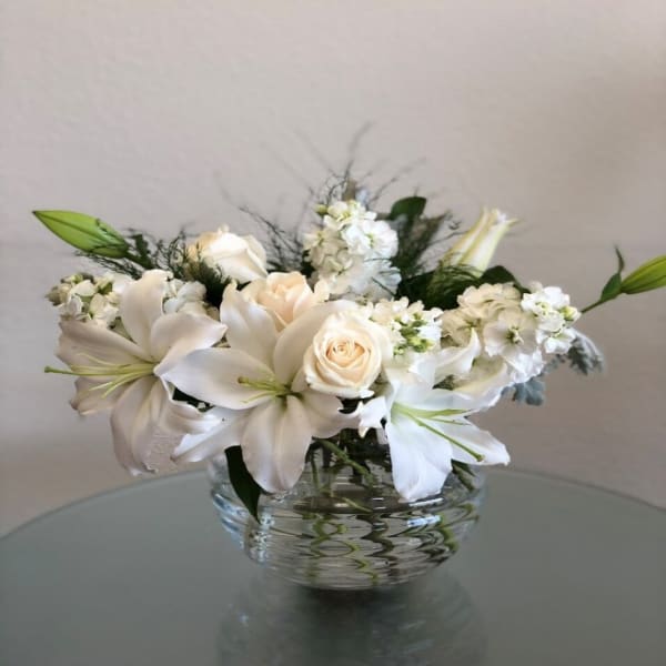 White lilies and roses arranged in a clear glass bowl vase