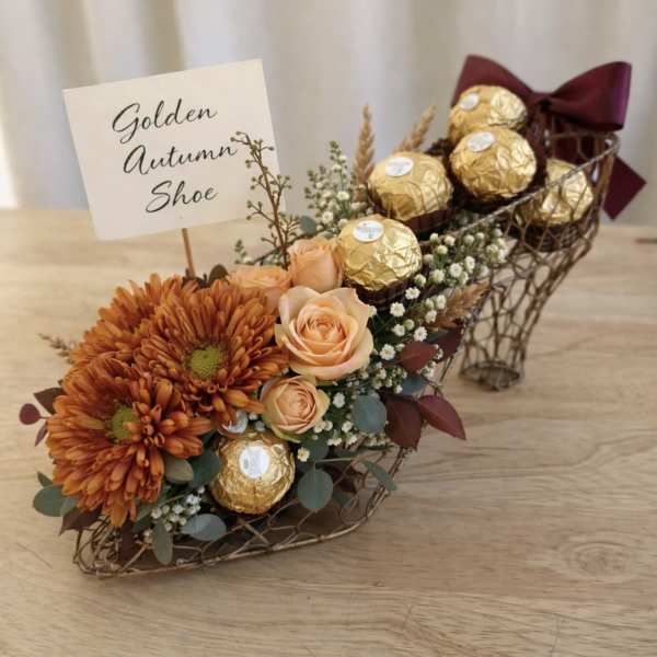 Orange flowers and gold chocolates arranged in a shoe-shaped basket