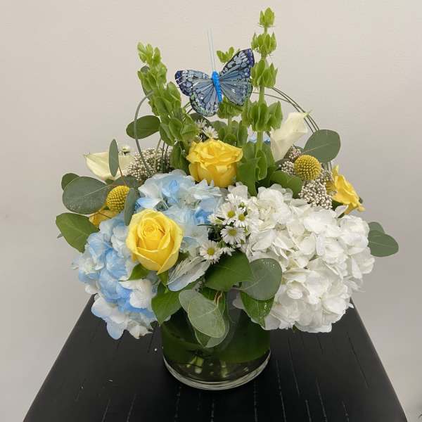 Blue and white hydrangeas with yellow roses in a glass vase