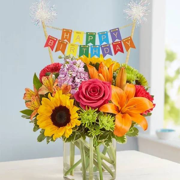 Birthday bouquet in a clear glass vase with a colorful banner topper
