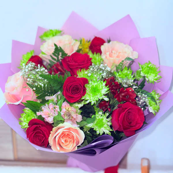 Bouquet of red and blush roses with green chrysanthemums in purple wrap