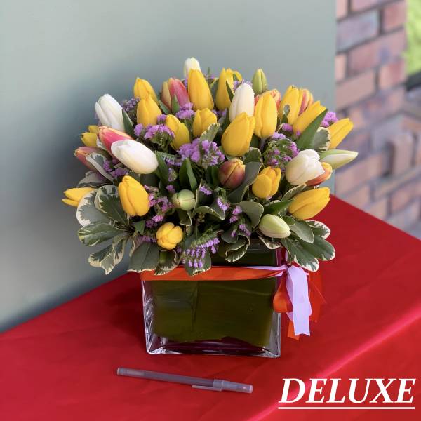 Yellow and white tulip bouquet in a square glass vase with purple filler