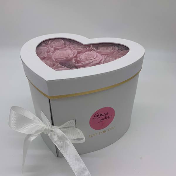 Heart-shaped white box filled with pink roses and tied with a white ribbon