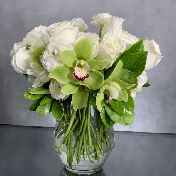 White roses and green orchids arranged in a clear glass vase
