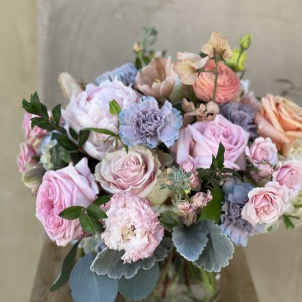 Pastel bouquet of roses, carnations, and blue flowers in a glass vase