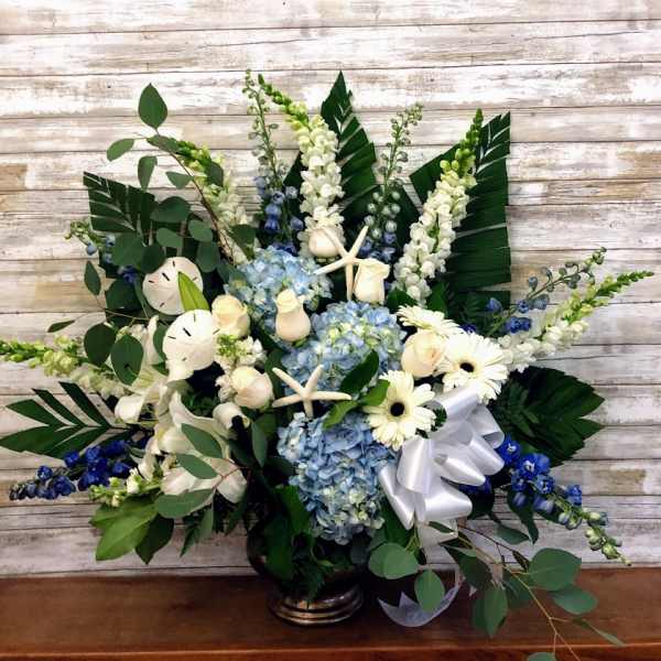 Blue hydrangeas and white flowers in a vase with a white ribbon