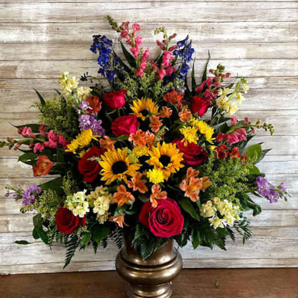 Large mixed flower arrangement in a gold vase with red, yellow, pink, and purple blooms