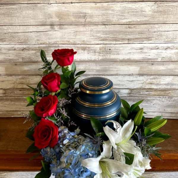 Red roses and white lilies arranged around a blue urn