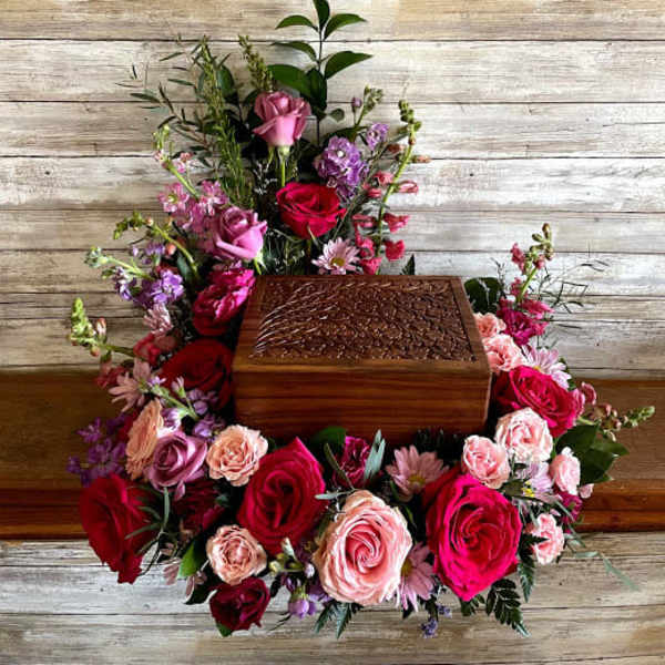Floral arrangement around a wooden urn box with pink and red roses