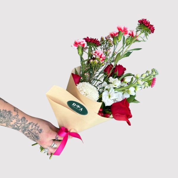 Hand-tied bouquet of red roses, white flowers, and pink carnations in kraft paper