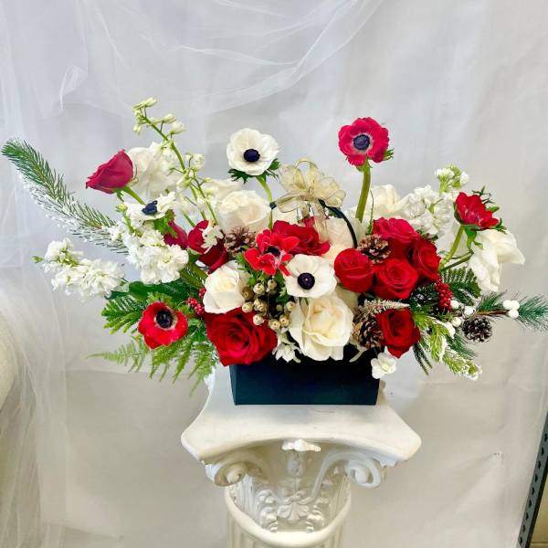 Red and white floral arrangement in a black box with a gold ribbon